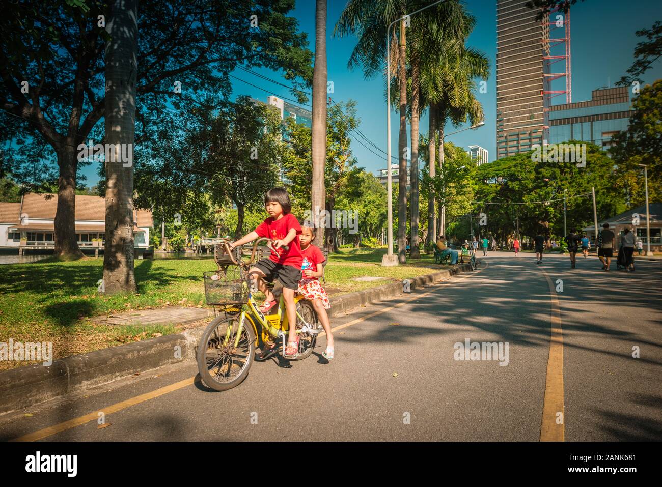 Bangkok/Thailand-06December2019: Lumphini park, morning view with two young girls riding a yellow bicycle on the road and tower building in background Stock Photo