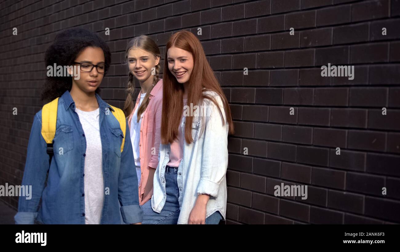 Caucasian teenagers laughing at afro-american schoolmate passing by, racism Stock Photo