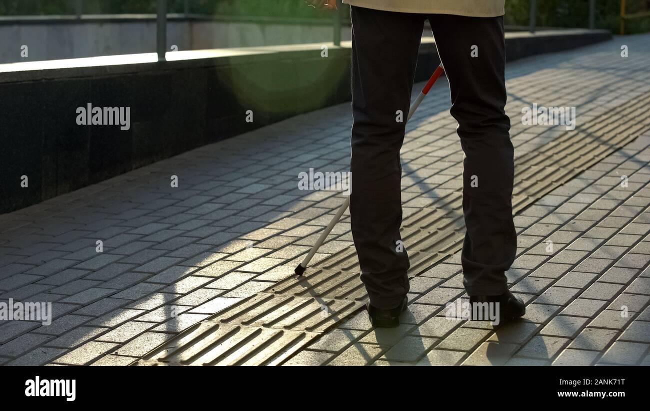 Visually impaired man with cane walking on special tactile paving for blind Stock Photo
