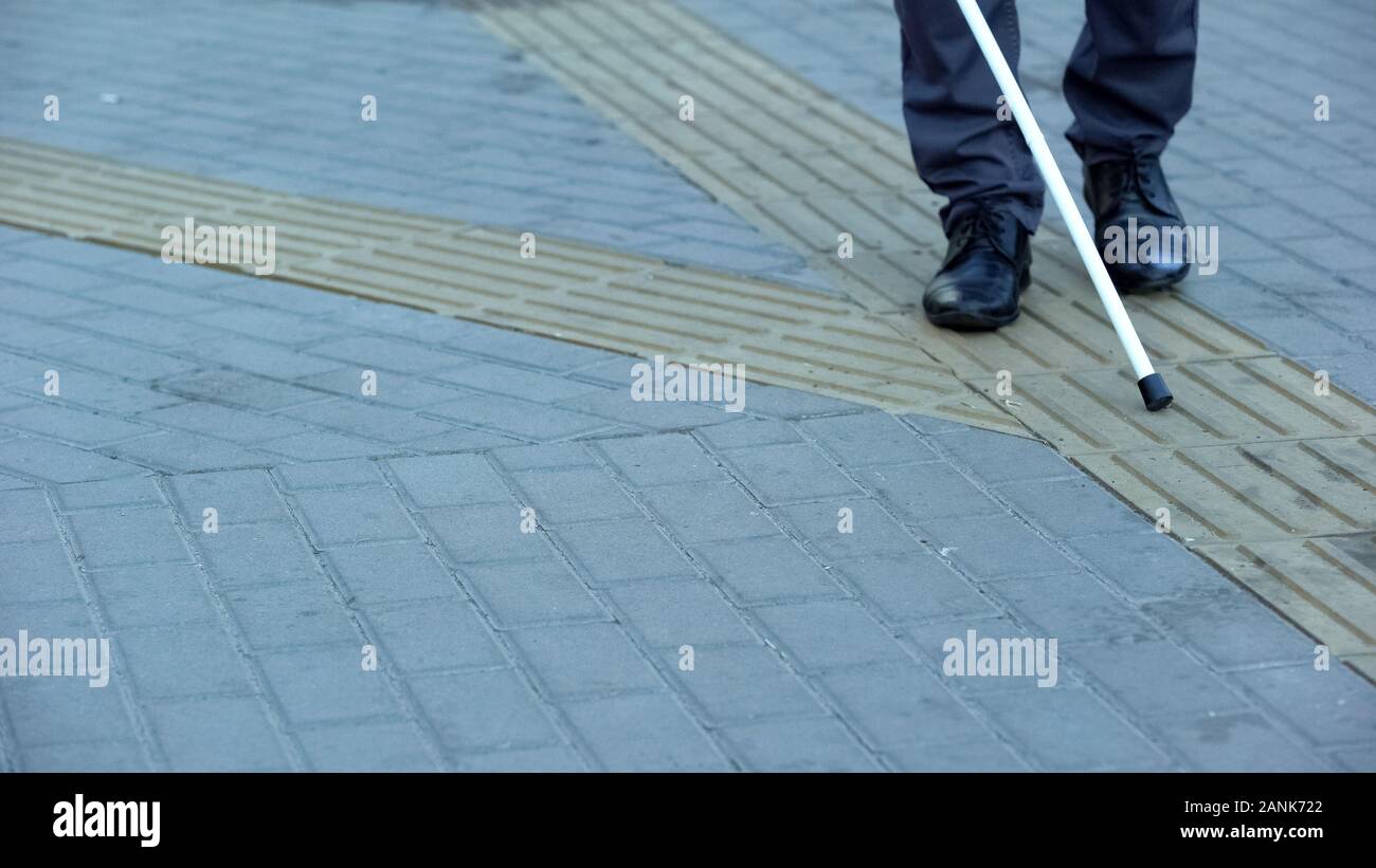 Blind man finds turn on tactile paving using walking stick, urban navigation Stock Photo