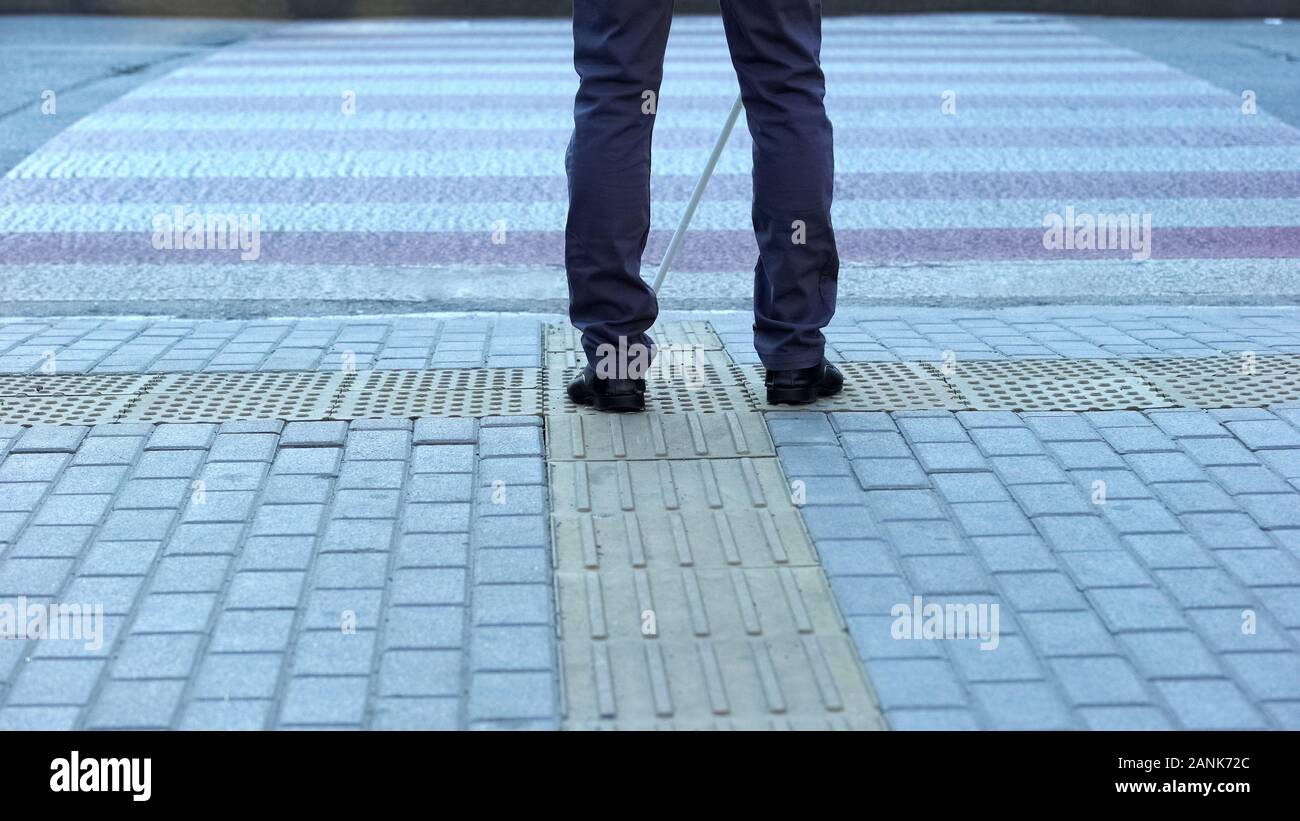 Lone blind man detecting tactile tiles, walking to pedestrian crossing safe road Stock Photo