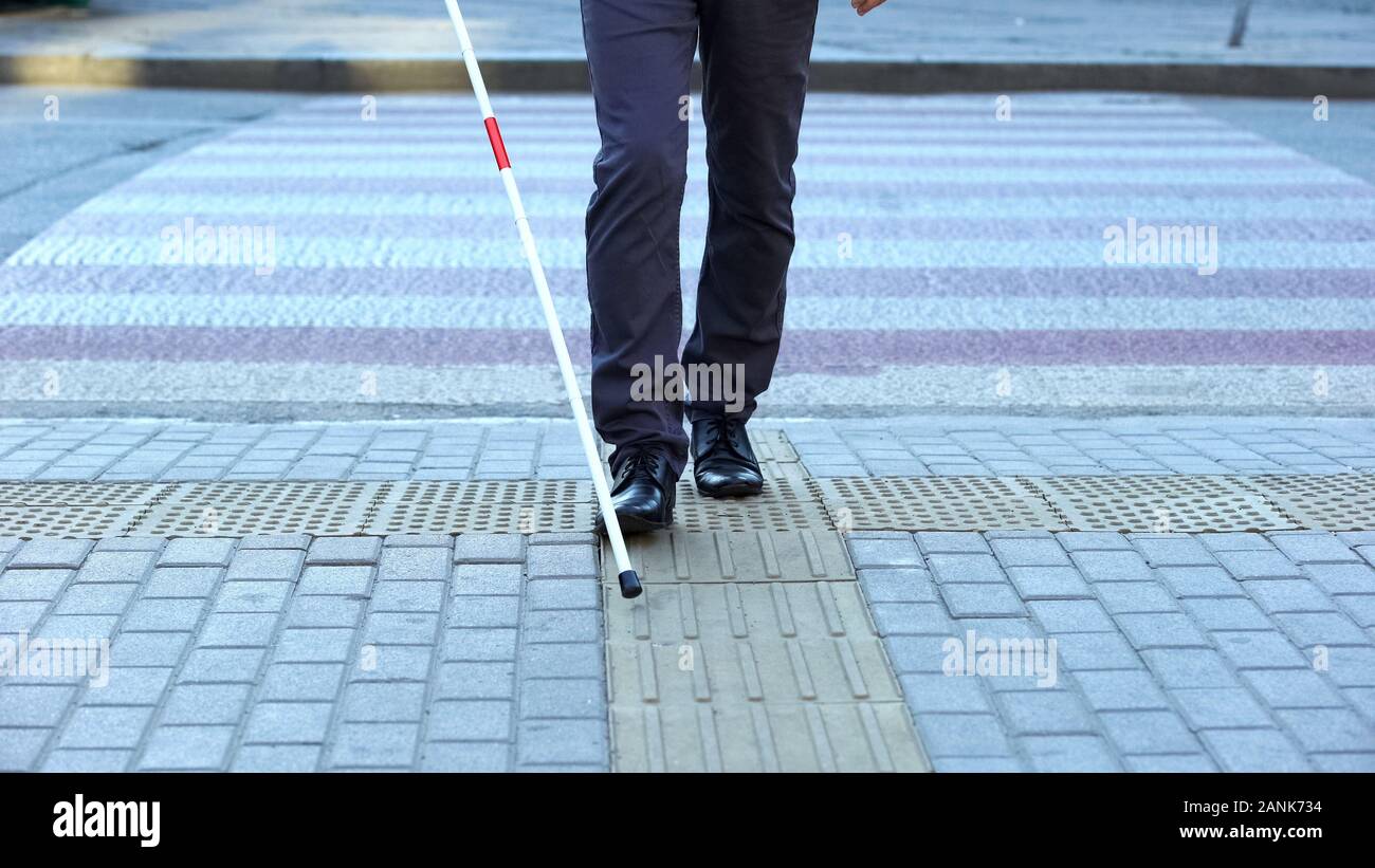 Visually impaired man using tactile tiles to navigate city, finishing crossroad Stock Photo