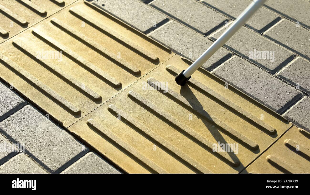 Blind person using white cane on straight tactile tiles to navigate road Stock Photo