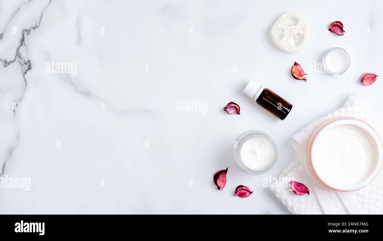 SPA natural organic essential oil, body cream, luffa sponge and tower on marble table with pink flower petals. Body care, clean skincare, SPA concept. Stock Photo
