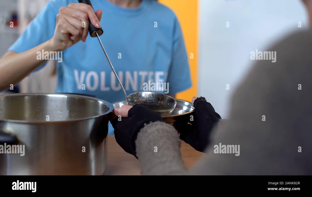 Charity project, female volunteer serving soup in shelter, care of poor people Stock Photo