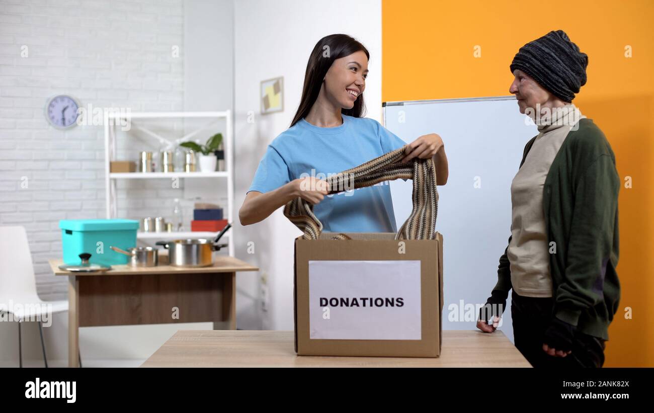 Female volunteer giving scarf poor woman from donation box, homeless