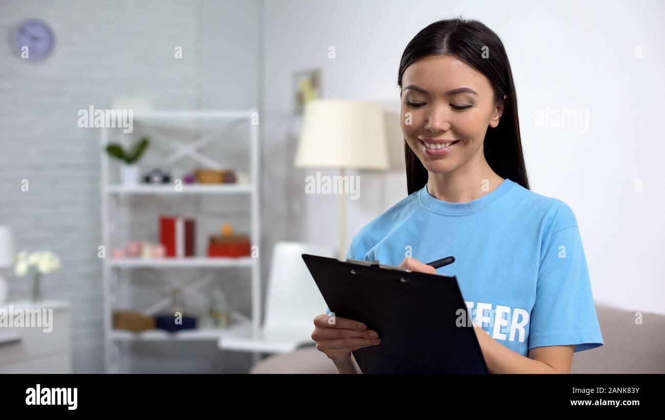 Female volunteer making notes and smiling, to-do list, charity project concept Stock Photo