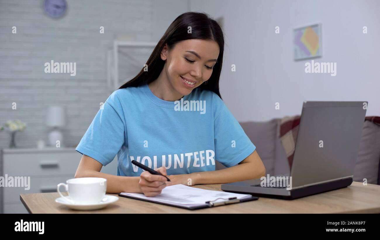 Female volunteer working laptop and writing notes sitting table, charity project Stock Photo