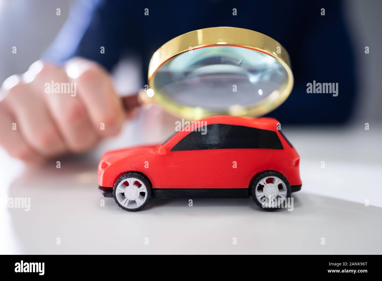 Businessman's Hand Holding Magnifying Glass Over Small Red Car Stock Photo