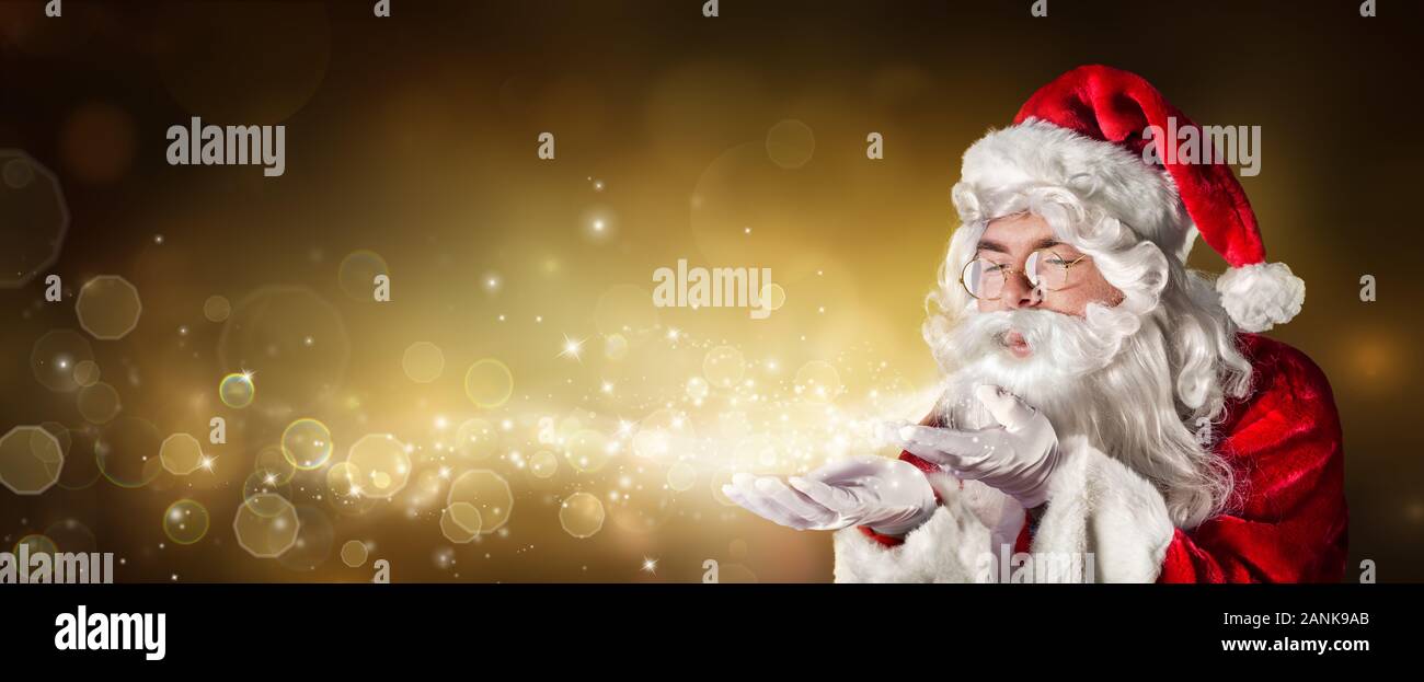 Santa Claus Blowing Magic Christmas Lights In Golden Background Stock Photo
