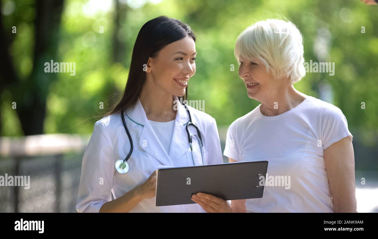 Smiling nurse showing elderly woman examination results in hospital park Stock Photo