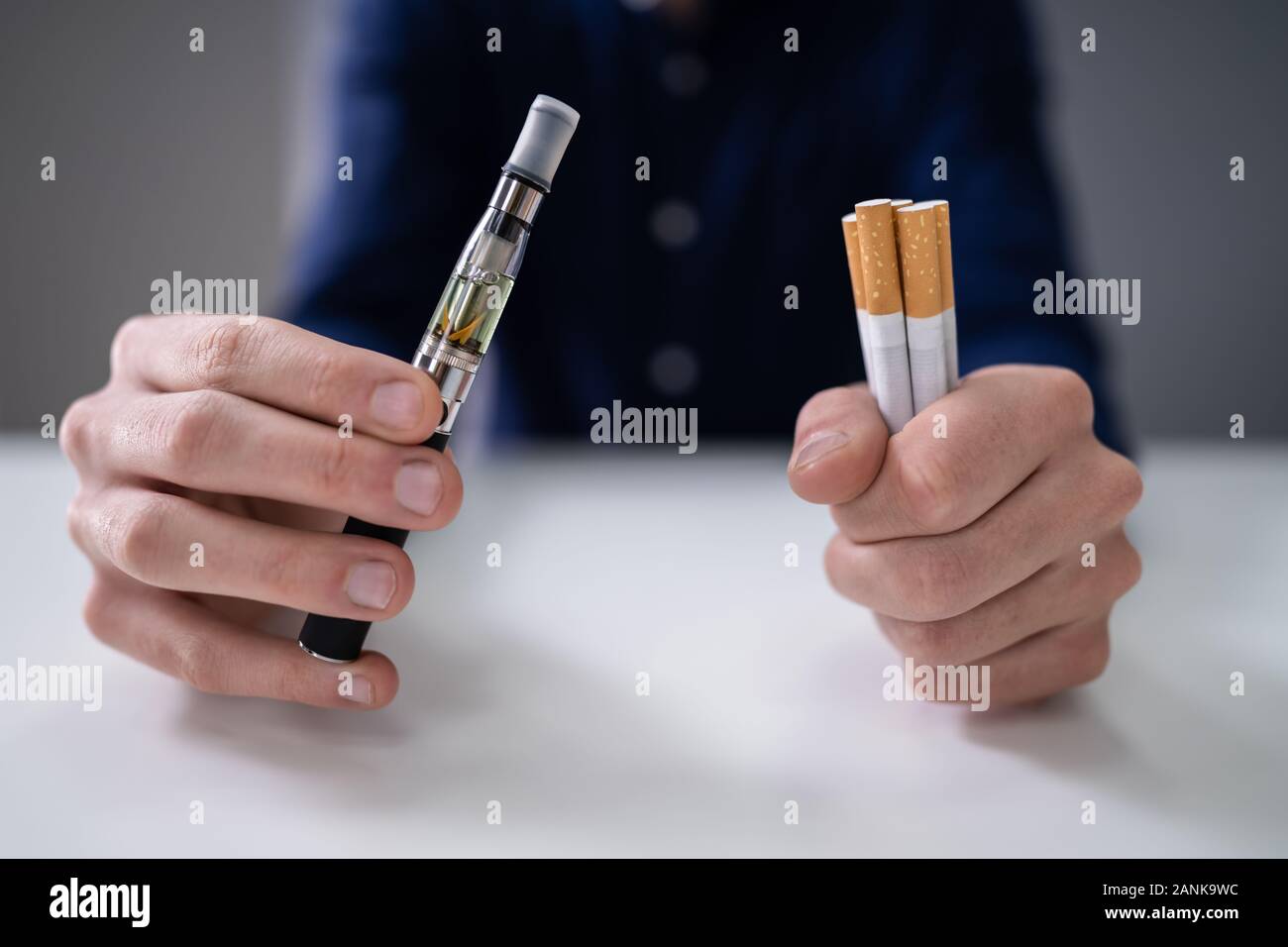 Man Holding Vape And Tobacco Cigarette Over Desk Stock Photo