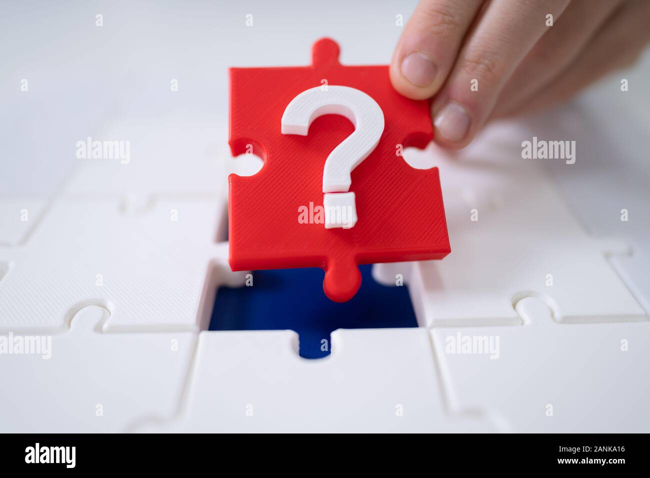 Close-up Of A Person's Hand Placing Red Question Mark Piece Into Jigsaw Puzzle Stock Photo