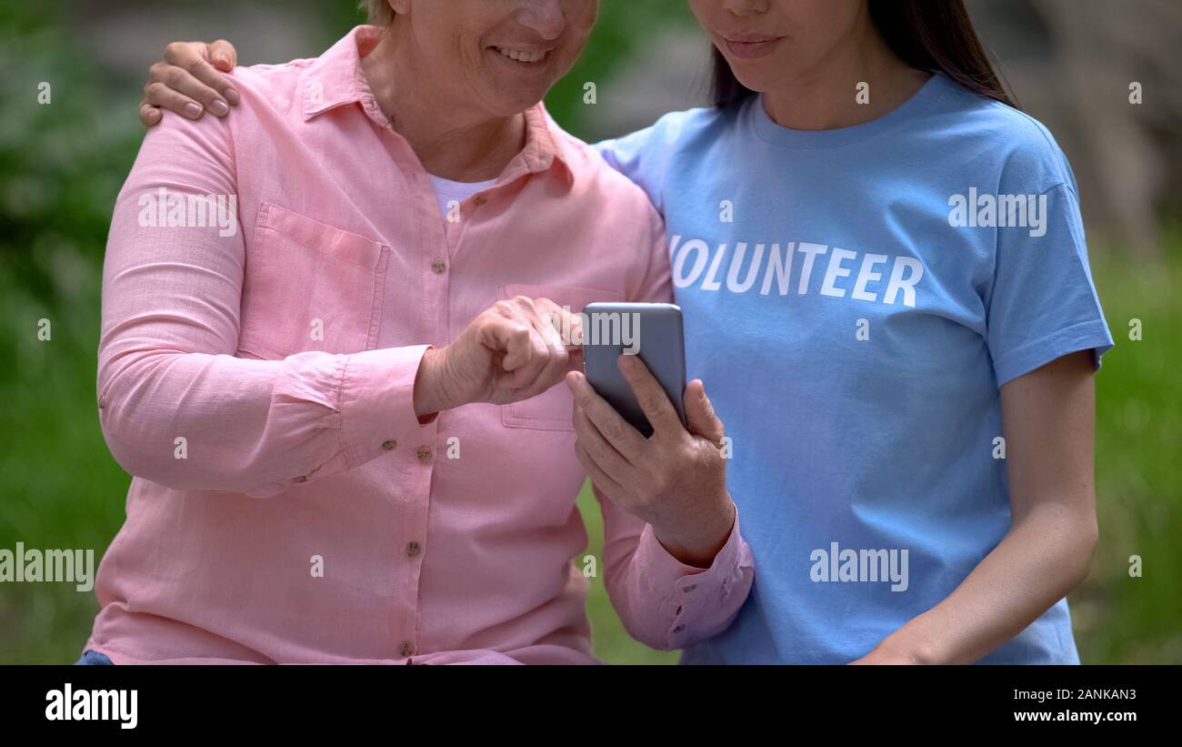 Mature woman and young volunteer looking smartphone photos together, assistance Stock Photo