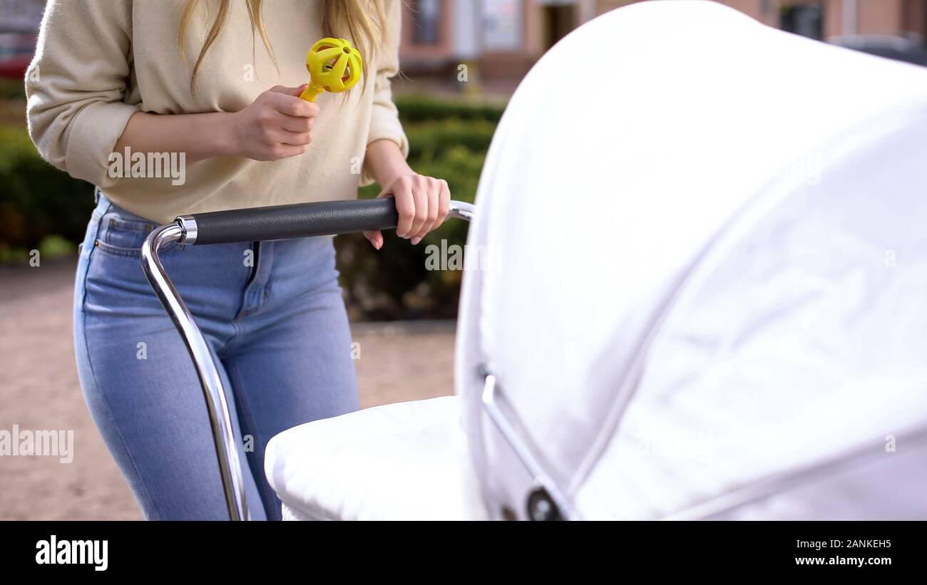 Woman holding rattle toy front of newborn in stroller, babyhood interaction Stock Photo