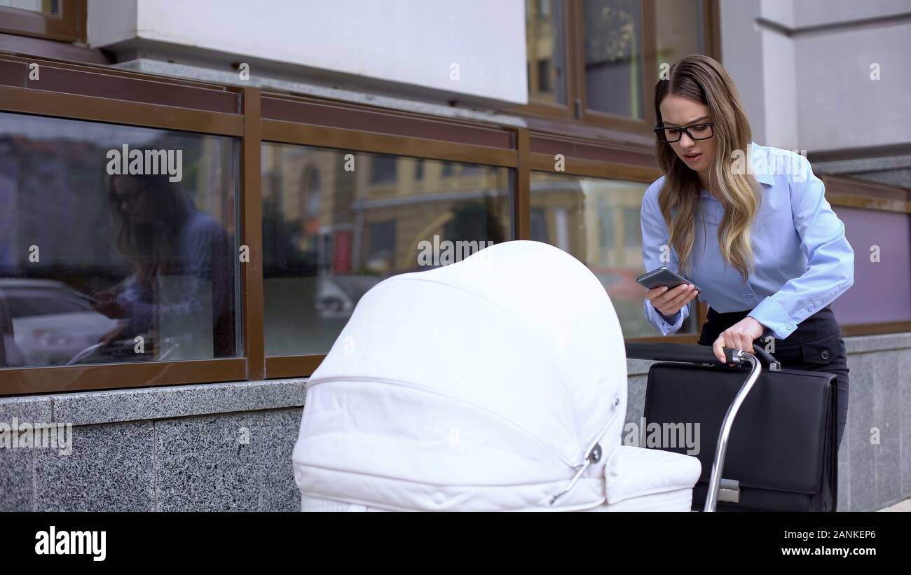 Multitasking business mother answering message as walking to work with baby pram Stock Photo