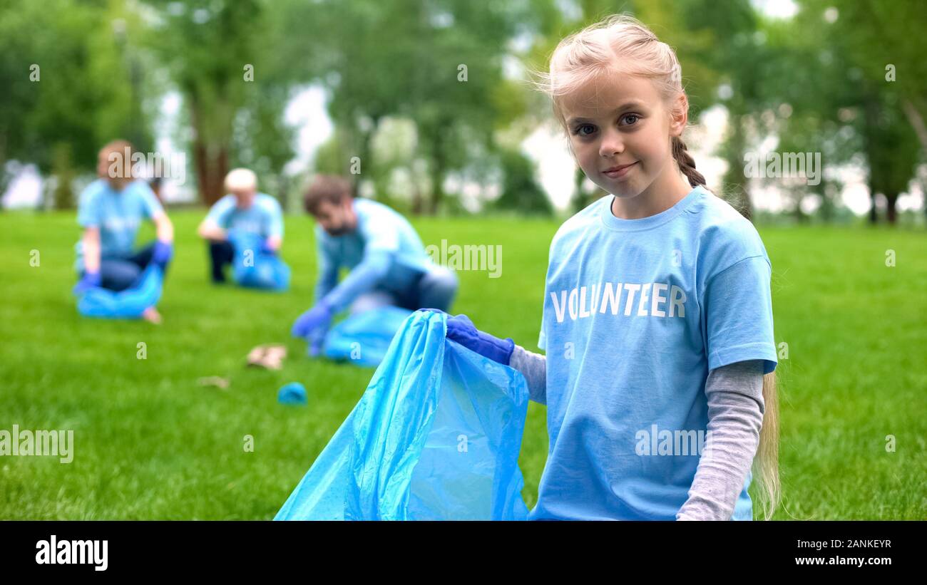 Responsible child volunteer collecting trash in garbage bag smiling on