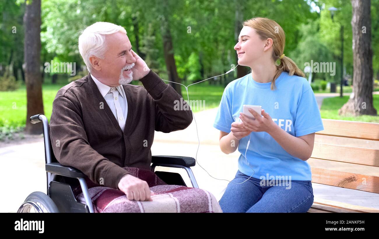 Happy young woman listening to music with old disabled man, supporting patient Stock Photo
