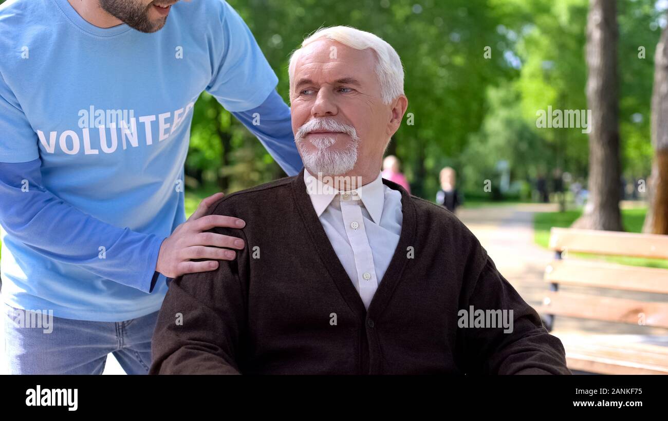 Male volunteer taking care of aged disabled patient, spending time in park Stock Photo