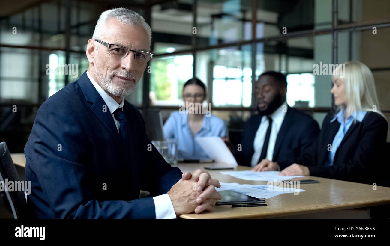 Elderly company director looking camera, office colleagues discussing ...