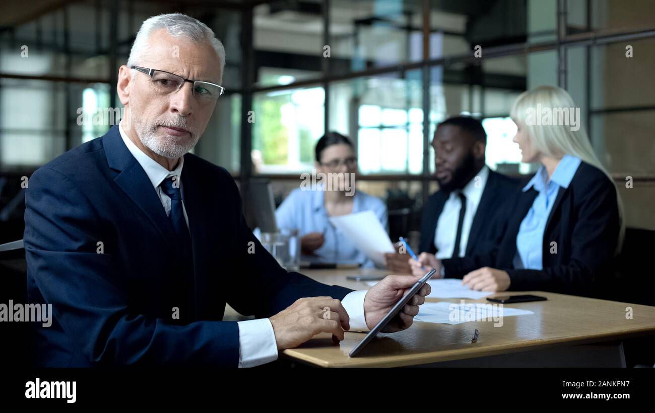 Concerned company boss making decision tablet in hands, managers discussing plan Stock Photo