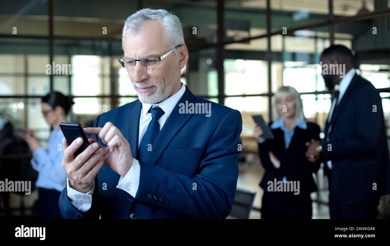 Mature male boss using smartphone, texting business partner, using mobile app Stock Photo