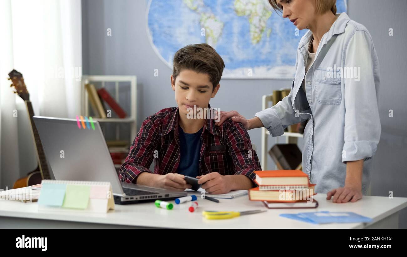 Mom talking to son using smartphone instead doing homework, generation gap Stock Photo