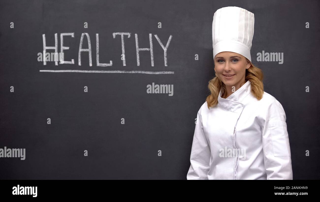 Professional chief cook smiling against blackboard with health word, nutrition Stock Photo