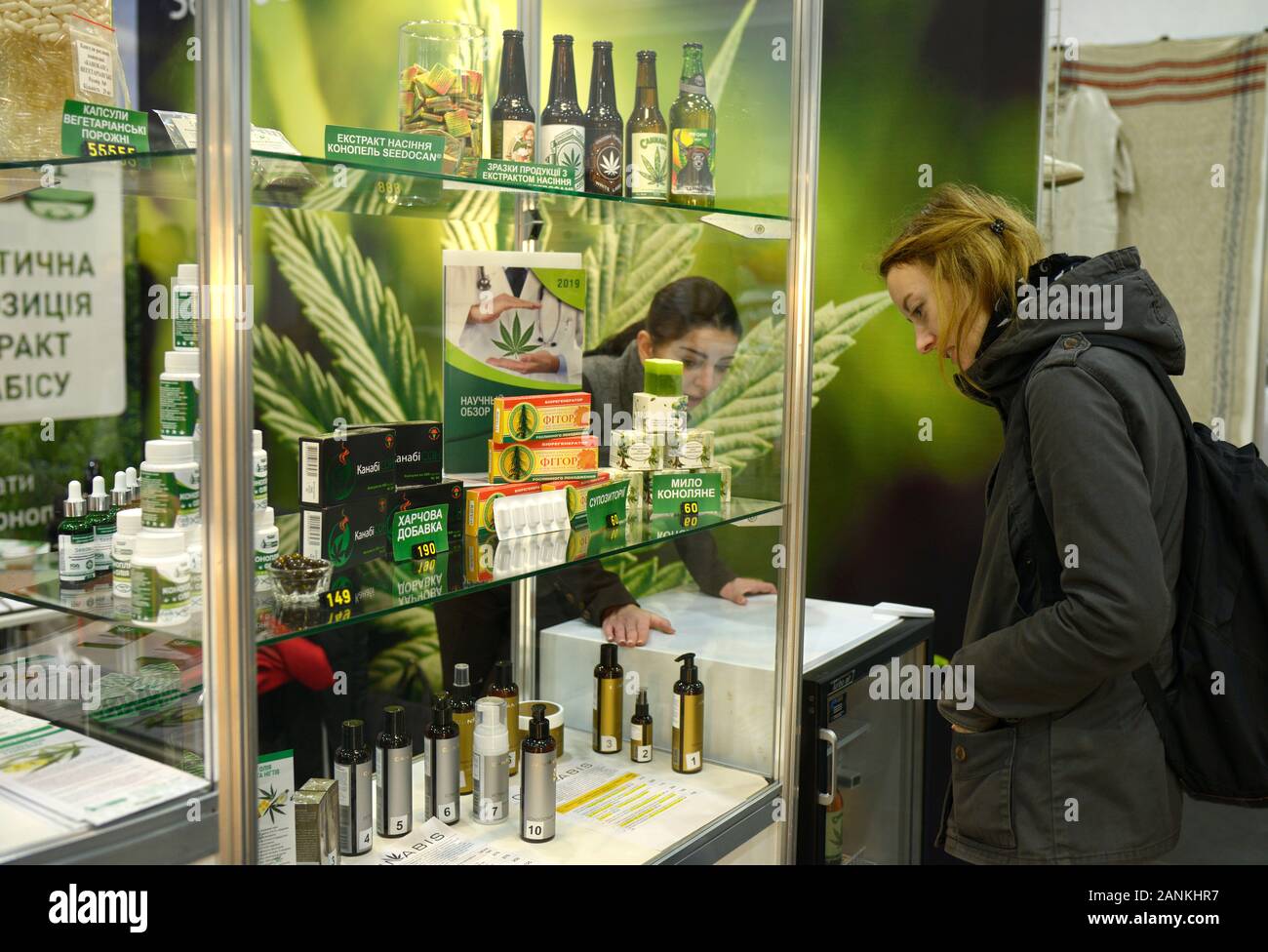 Young woman standing in front of counter with cannabis products (oil, beer, soap, food additives) and talking to seller.October 11,2019. Kiev, Ukraine Stock Photo