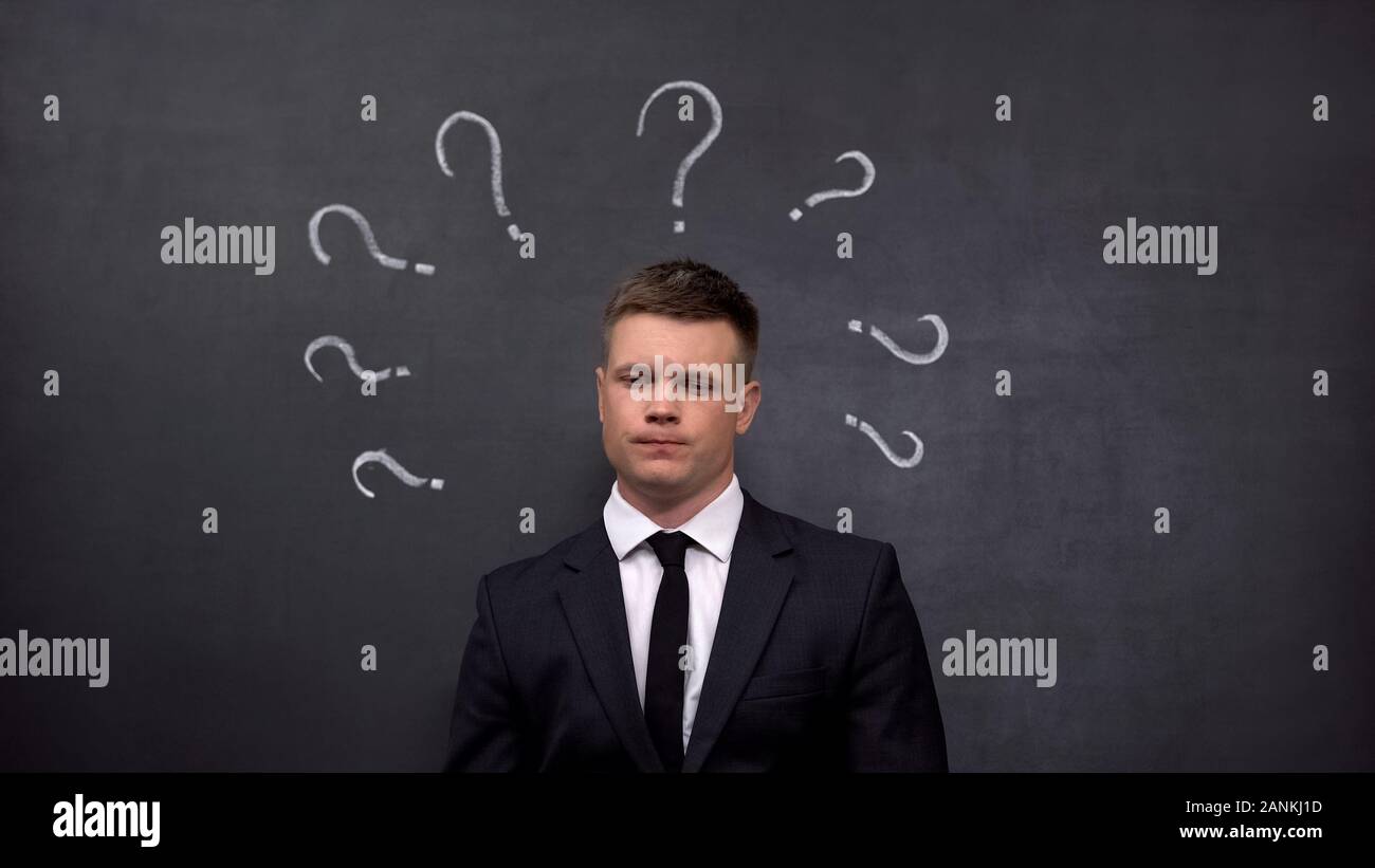 Doubtful businessman lacking ideas, question marks painted on blackboard, answer Stock Photo