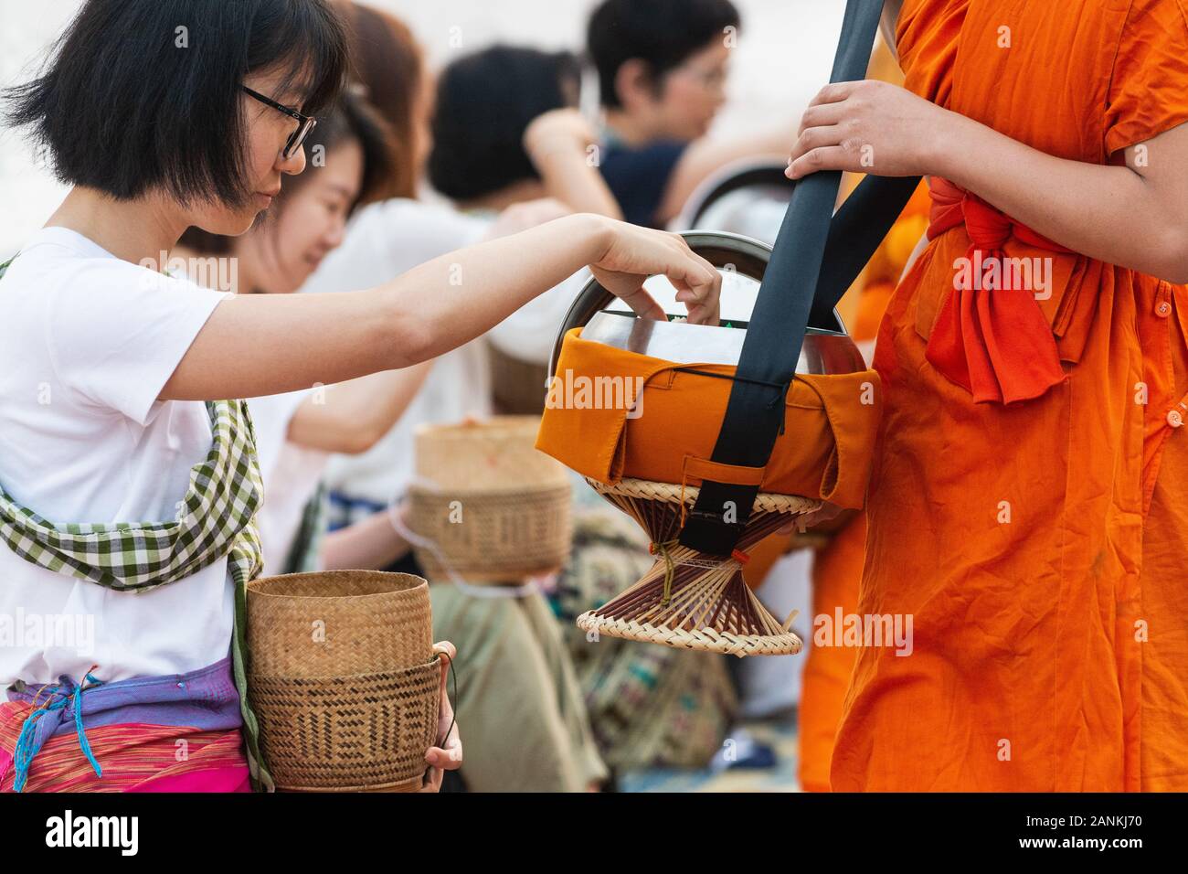 Luang Prabang, Laos - May 2019: Laotian woman making offerings to Buddhist monks during traditional morning alms giving ceremony Stock Photo
