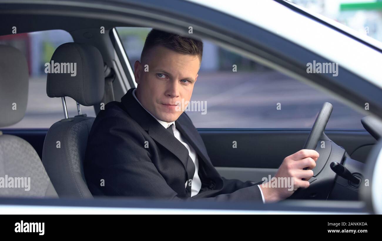 Displeased man in suit sitting on driver seat, looking for client, taxi services Stock Photo