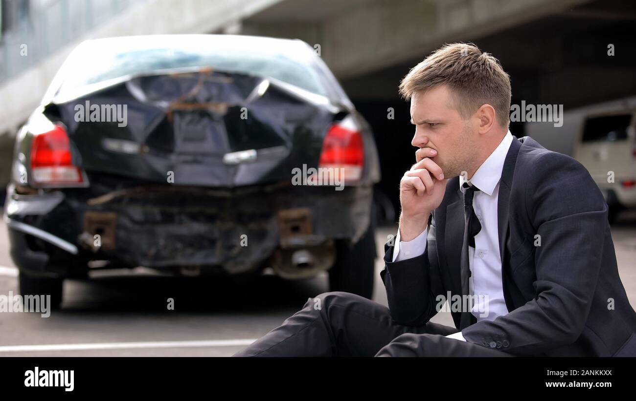 Frustrated man sitting road on crashed car background, traffic accident  stress Stock Photo - Alamy