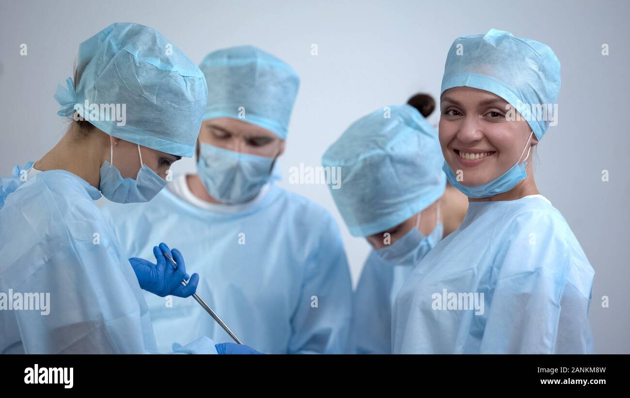 Professional surgeon team working in operation room, nurse smiling at camera Stock Photo