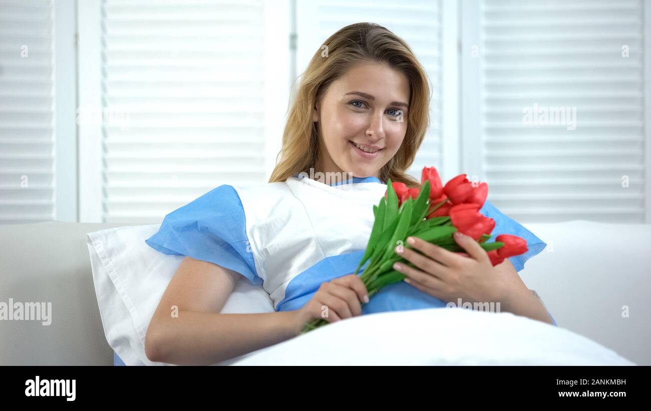 Happy mother holding flowers bunch lying in hospital after giving birth to baby Stock Photo