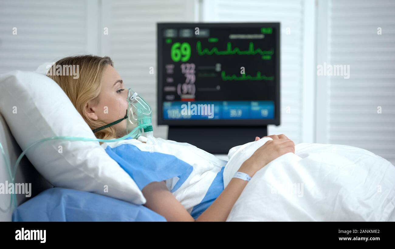 Crying woman in reanimation waking up after abortion, ecg monitor in room Stock Photo