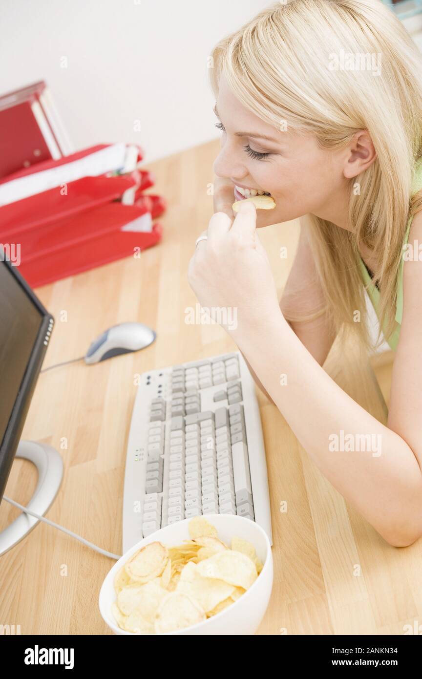 Junge Frau isst Chips am Schreibtisch - Young woman eating chips at desk Stock Photo