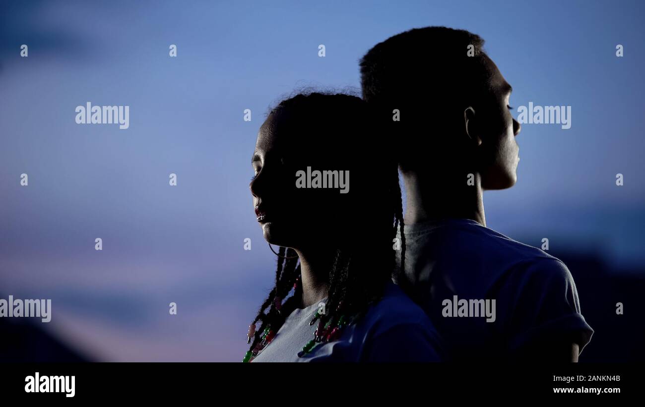 Couple standing to each other back in darkness, confronting problems together Stock Photo