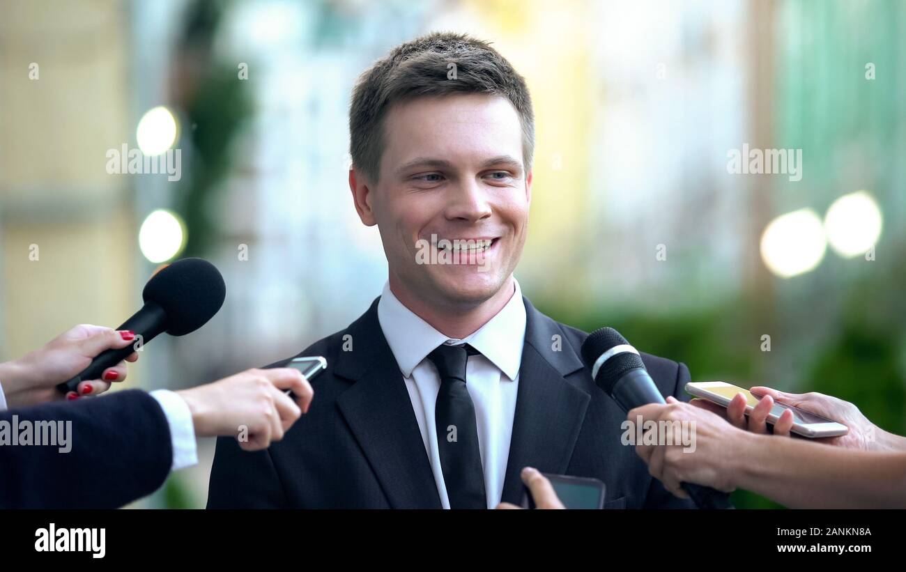 Smiling man in suit giving interview to journalists, evening news broadcasting Stock Photo