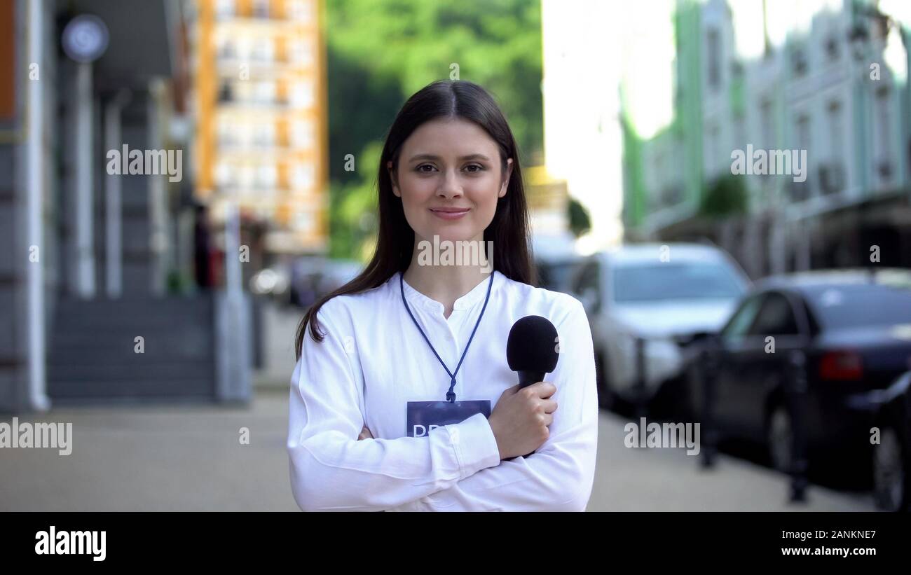 Female journalist with microphone and press pass looking at camera on street Stock Photo