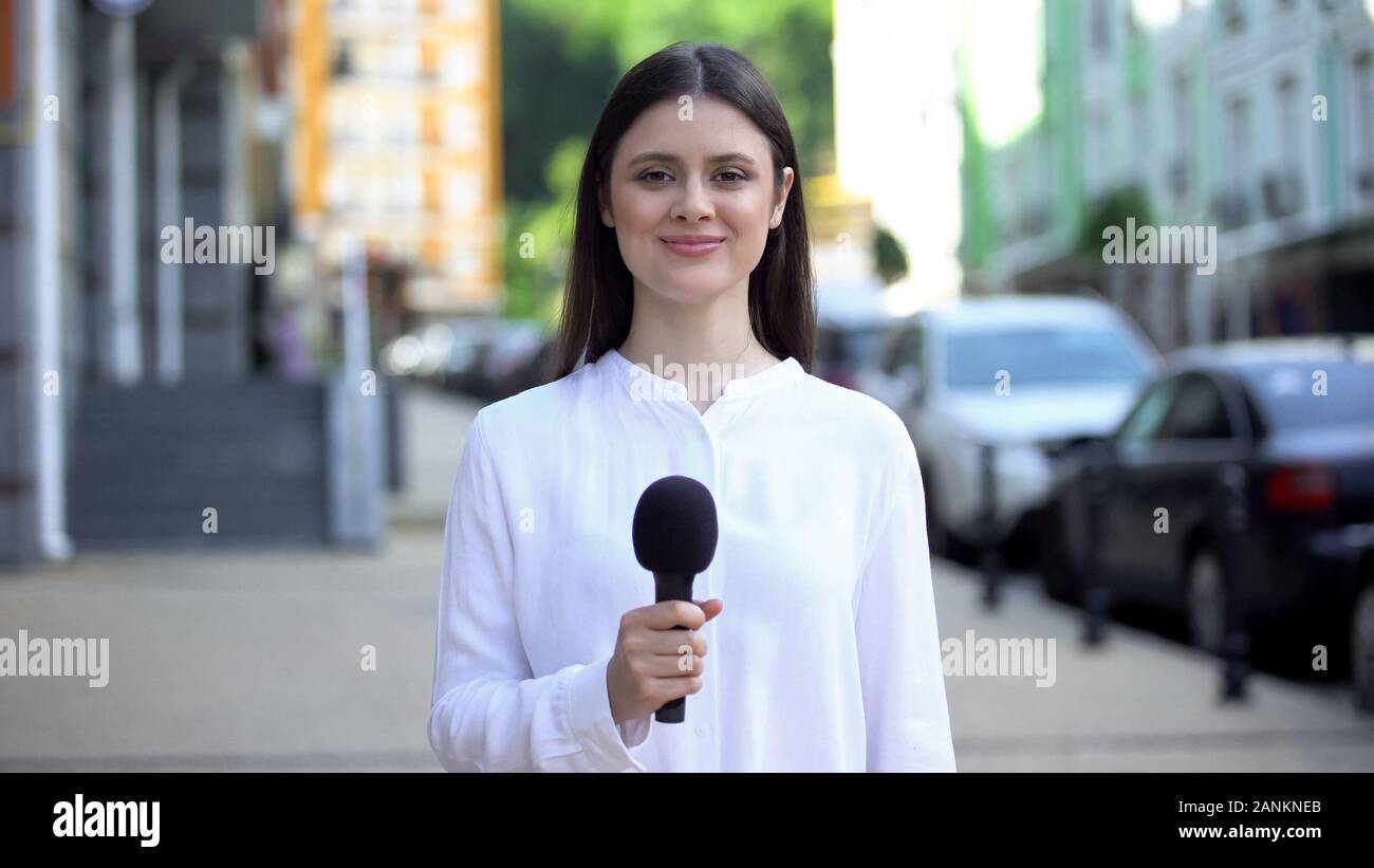 Cheerful female reporter holding microphone and smiling at camera, interview Stock Photo