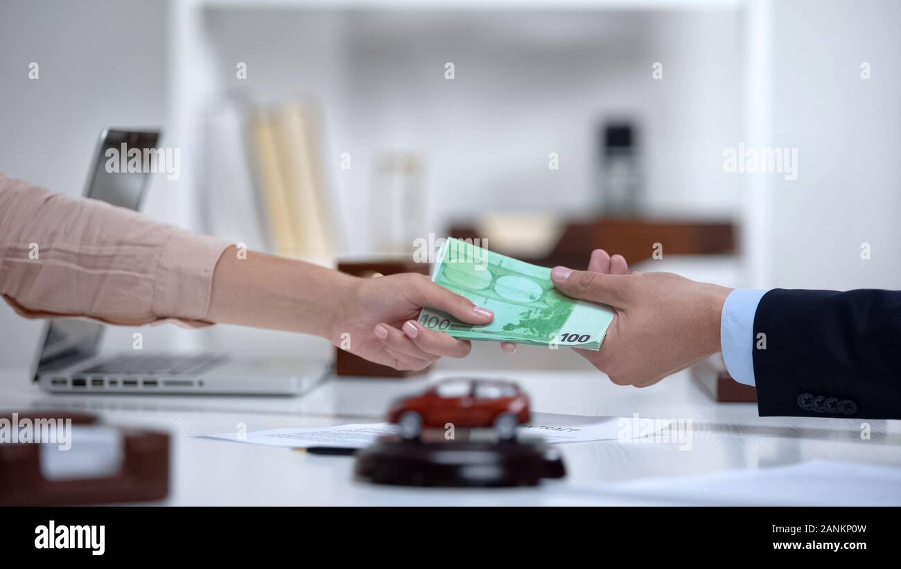 Woman giving euro money to car dealer, down payment on latest electric vehicle Stock Photo