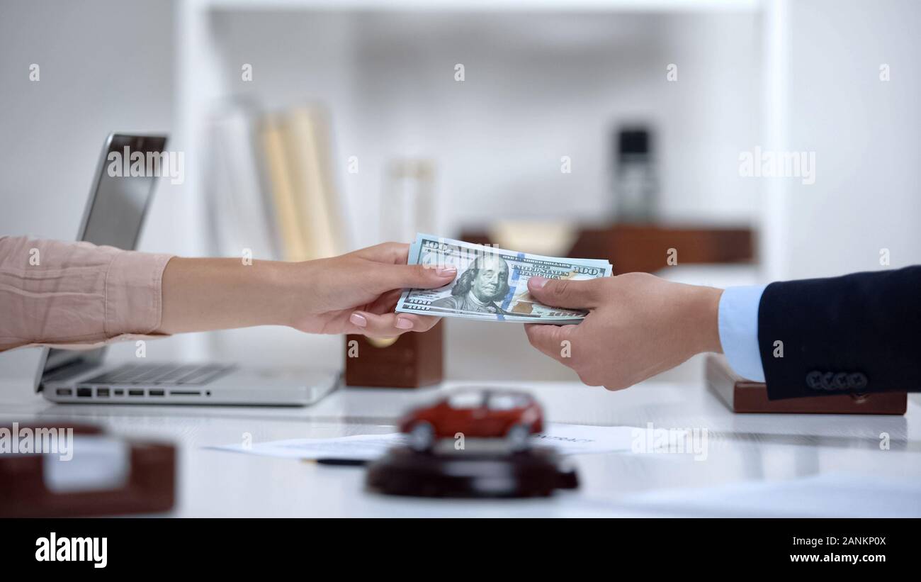 Female giving dollars to car dealer, down payment on brand new electric vehicle Stock Photo