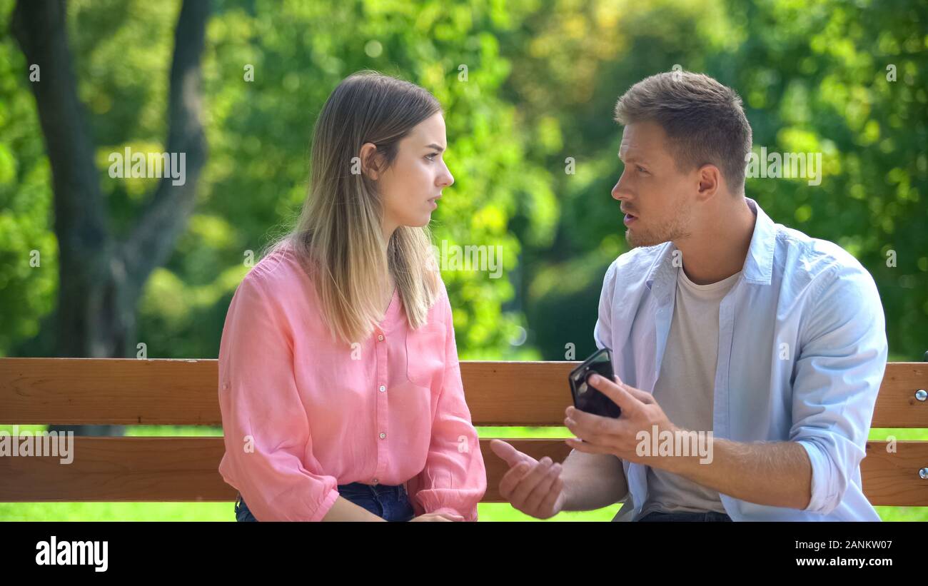 Guy with girlfriend phone feeling jealous, relations distrust, misunderstanding Stock Photo