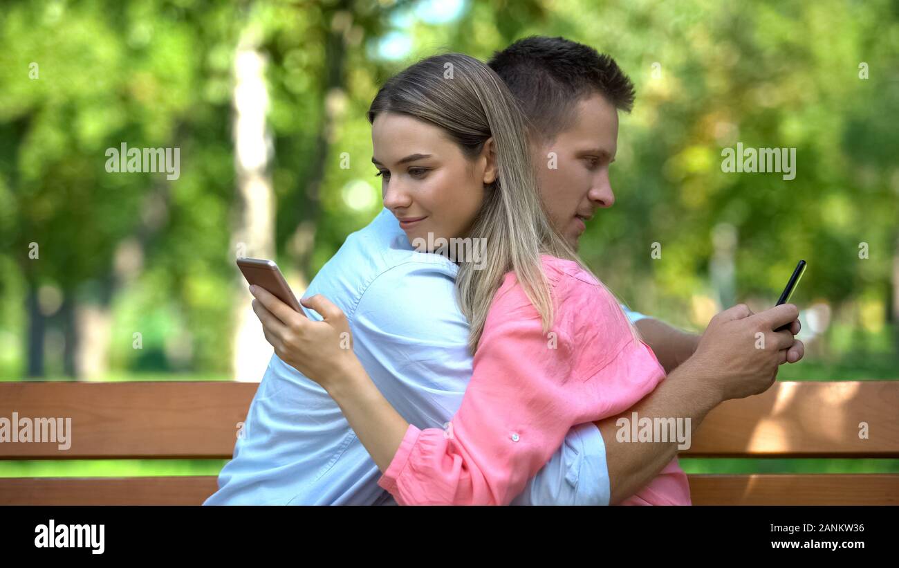 Young couple hugging at park chatting on smartphones, lack of communication Stock Photo