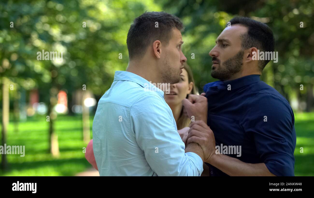 Angry boyfriend pushing man fighting outdoors, girlfriend trying to calm down Stock Photo
