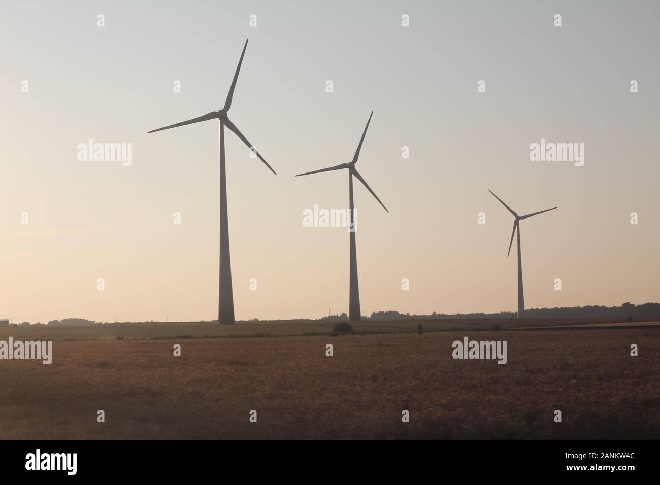 Three windmills, wind turbines standing in the field in the sunset Stock Photo Alamy