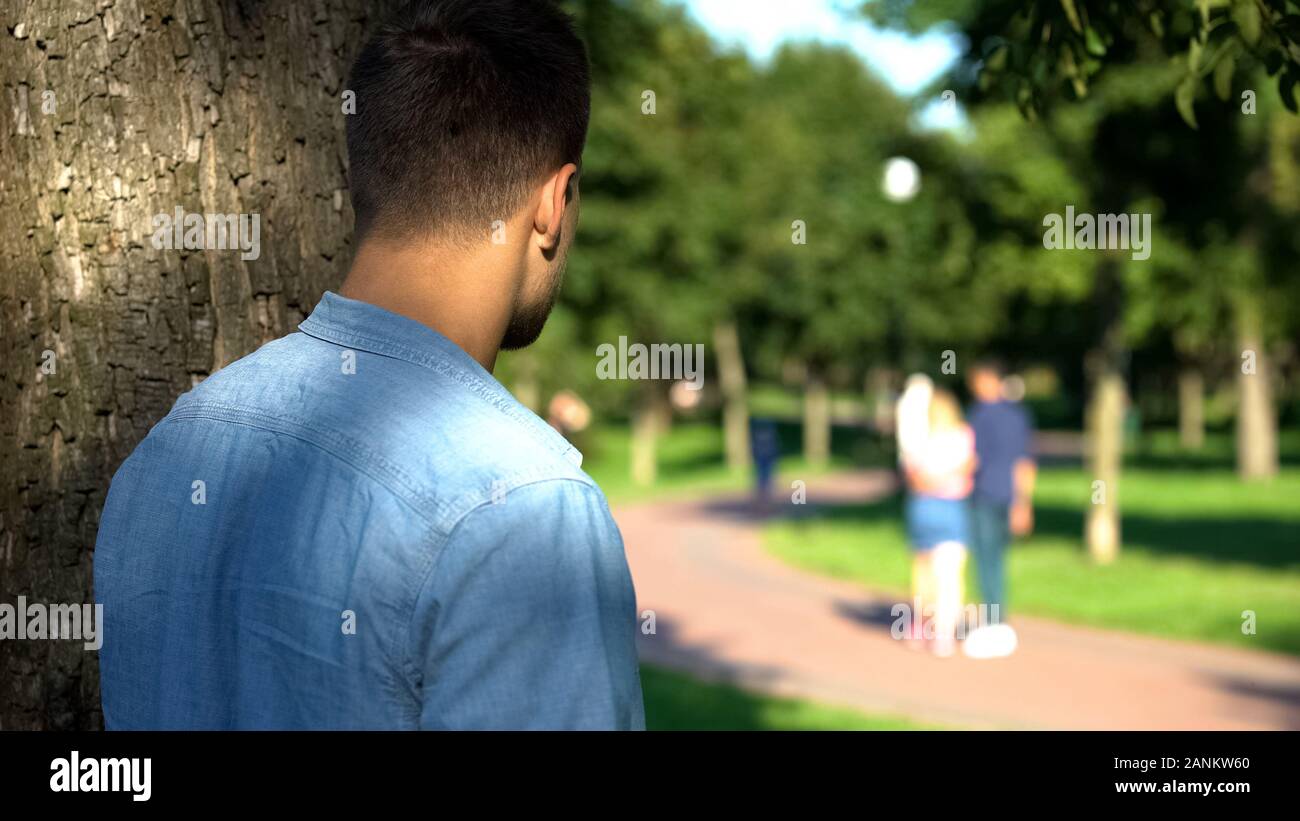 Man secretly spying loving couple walking on date outdoors, jealous ex-boyfriend Stock Photo