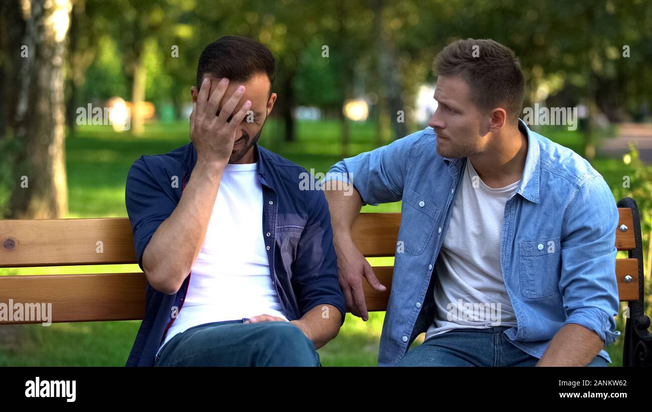 Man comforting sad male friend sitting on bench in park, life problems
