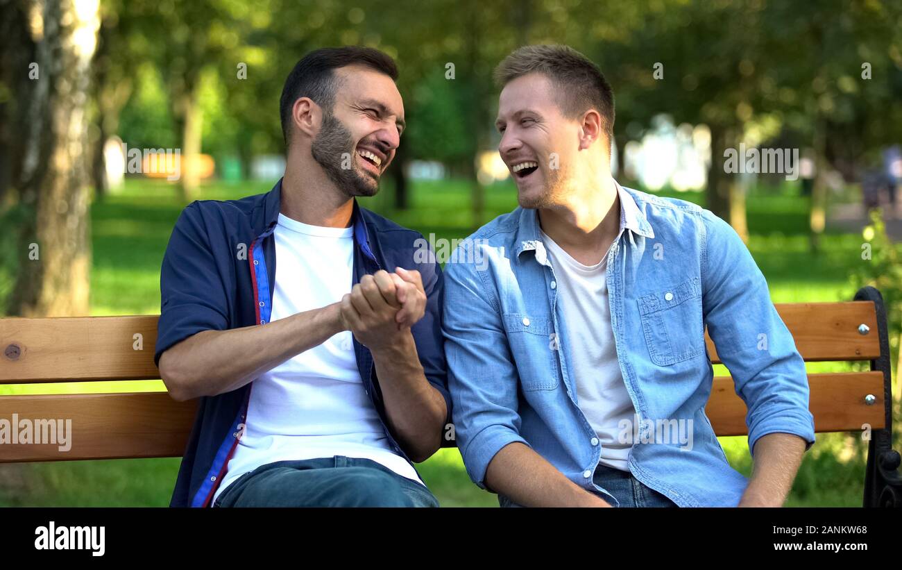 Male friends joking and laughing on bench in park, friendship togetherness Stock Photo